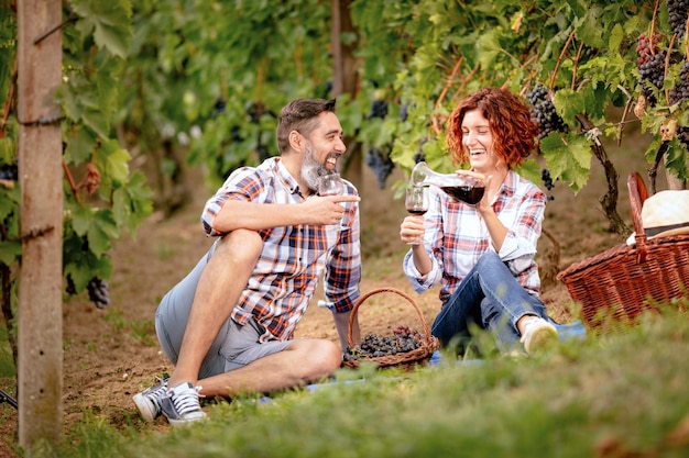 Beautiful smiling couple having picnic and tasting wine at a vineyard.