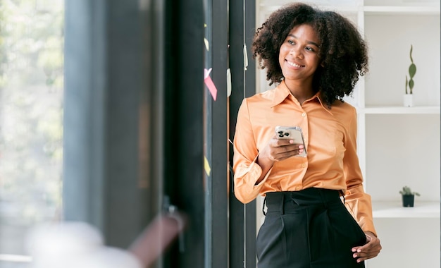 Beautiful smiling curlyhaired businesswoman using smarphone indoors copy space