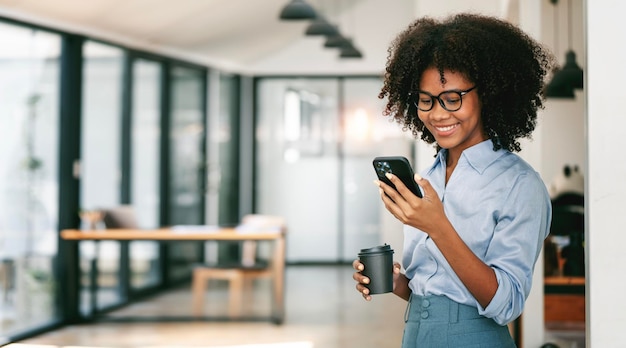 Beautiful smiling curlyhaired businesswoman using smarphone in office copy space