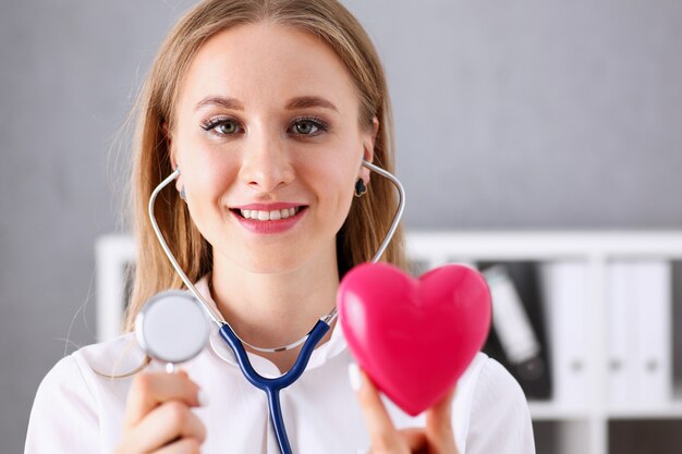 Beautiful smiling doctor hold in arms red heart