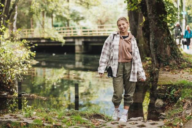 Beautiful smiling female teenager taking a break and relaxing by the mountain river during  walk in nature.