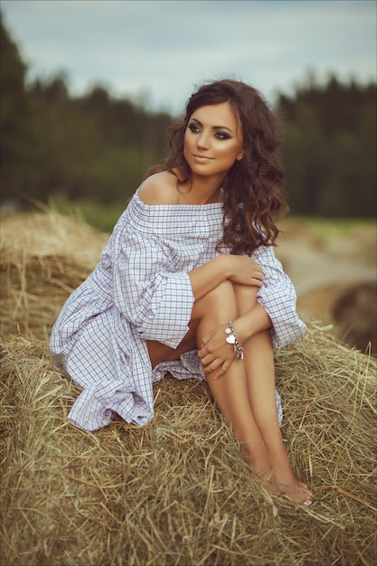 Beautiful smiling girl near a hay bale in the countryside. Girl sitting on the haystack