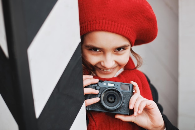 Beautiful smiling girl in a red beret takes pictures on the city street. High quality photo