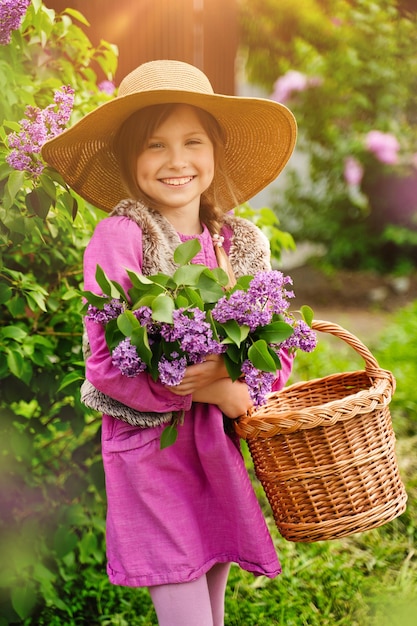 Beautiful smiling girl in straw hat in lilac Garden Girl with lilac flowers in springtime Gardening