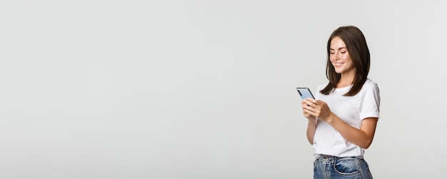 Beautiful smiling girl using mobile phone looking at smartphone pleased