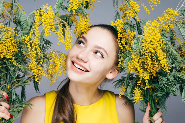 Beautiful smiling girl in a yellow dress enjoying the spring and fragrant mimosa