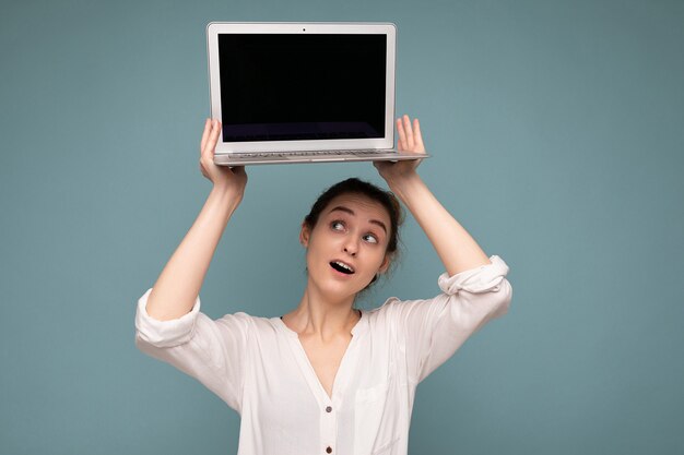 Beautiful smiling happy young woman holding computer laptop looking up at netbook having fun wearing casual smart clothes isolated over wall background. Mock up, copy space, cutout