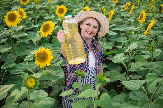 Beautiful smiling joyful middleaged farmer woman holding bottles of golden sunflower oil in her hands in a harvest field of sunflowers on a sunny day