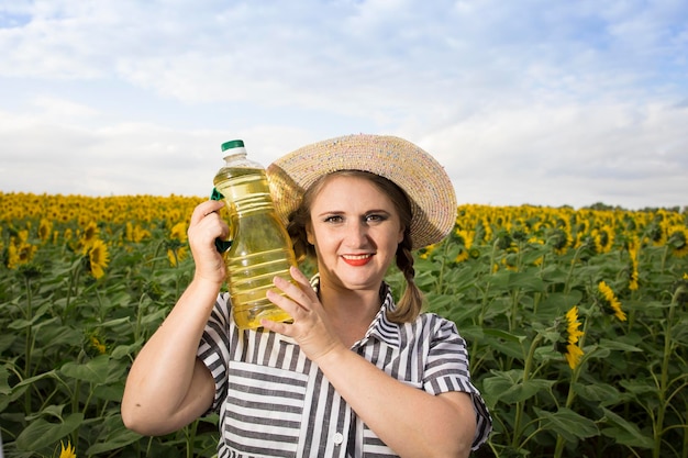 Beautiful smiling joyful middleaged farmer woman holding bottles of golden sunflower oil in her hands in a harvest field of sunflowers on a sunny day