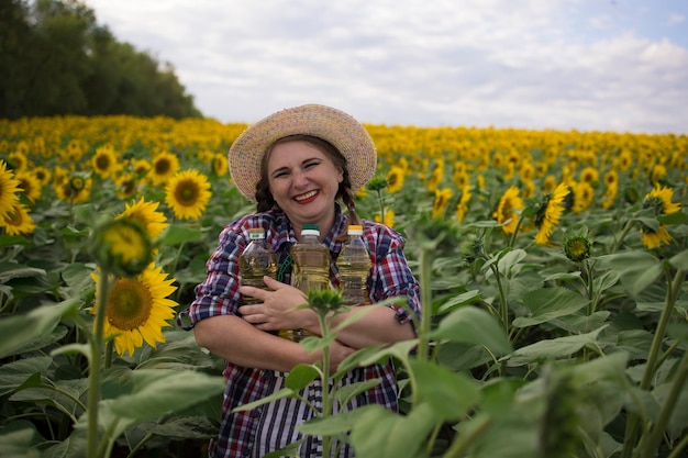 Beautiful smiling joyful middleaged farmer woman holding bottles of golden sunflower oil in her hands in a harvest field of sunflowers on a sunny day