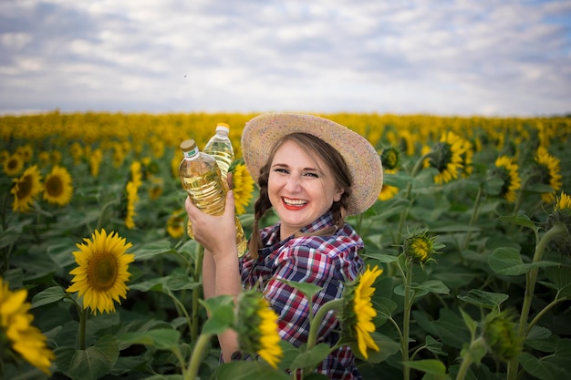 Beautiful smiling joyful middleaged farmer woman holding bottles of golden sunflower oil in her hands in a harvest field of sunflowers on a sunny day