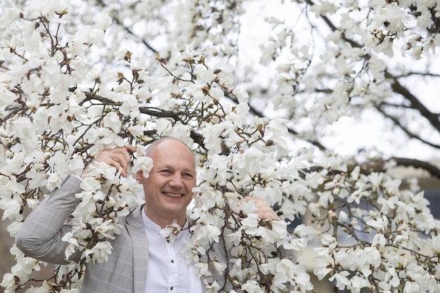 Beautiful smiling man on the background of white flowering magnolia