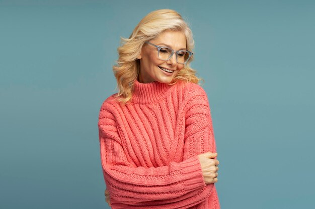 Beautiful smiling mature woman wearing winter sweater and stylish eyeglasses looking away in studio