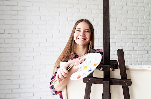 Photo beautiful smiling woman artist with color palette and paintbrushes