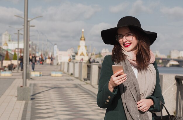 Beautiful smiling woman in glasses wears trendy outfit using mobile phone. Outdoor lifestyle portrait