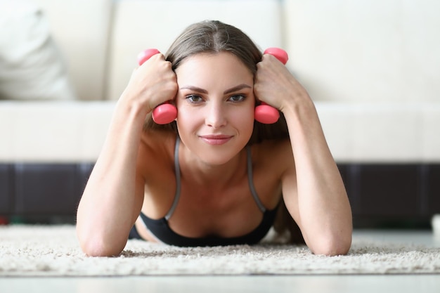 Beautiful smiling woman lies and holds dumbbells closeup