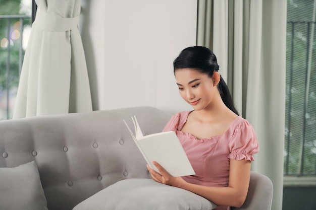 Beautiful smiling woman reading a book and lying on the sofa in the living room