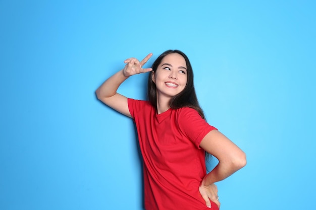 Beautiful smiling woman showing victory gesture on color background