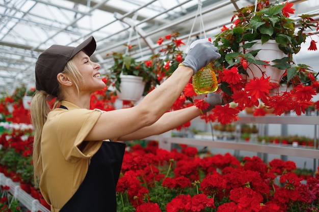 Beautiful smiling woman spraying plants at flower center