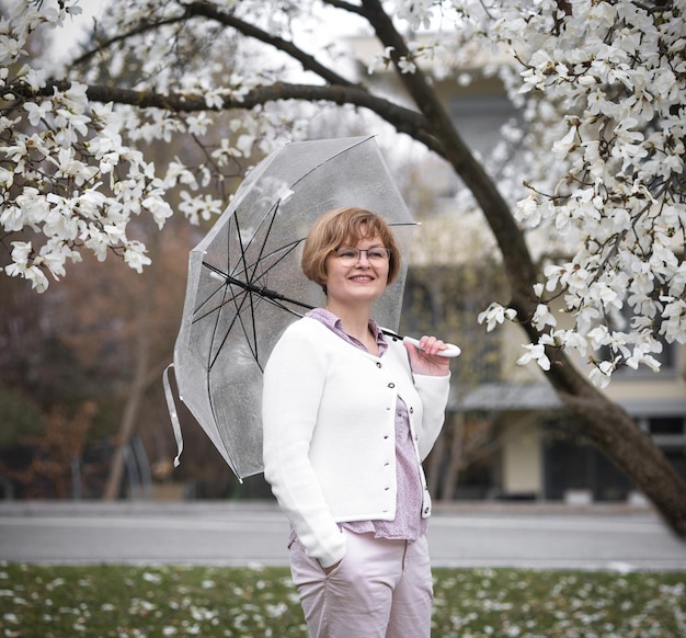 Beautiful smiling woman umbrella against background white flowering magnolia