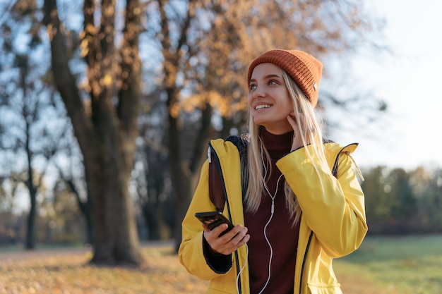 Beautiful smiling woman wearing raincoat hat listening music in park autumn inspiration travel