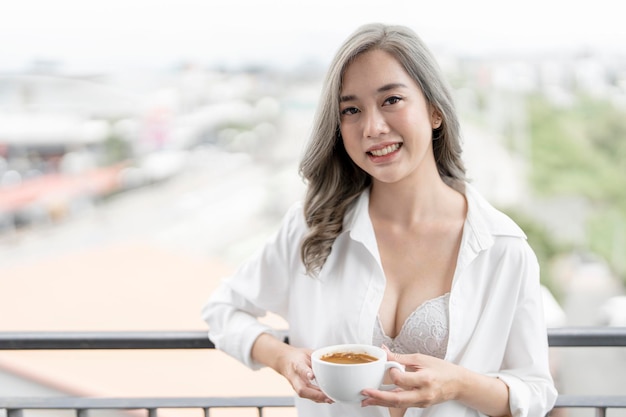 Beautiful smiling woman in white lingerie holding cup of coffee relaxing at home in the morning