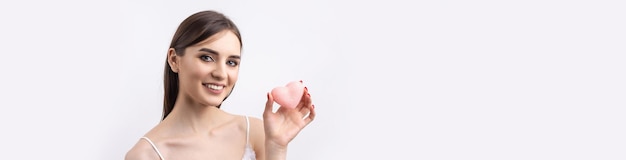 Beautiful smiling woman with clean skin natural makeup and white teeth on a gray background Holding a pink hygienic heart