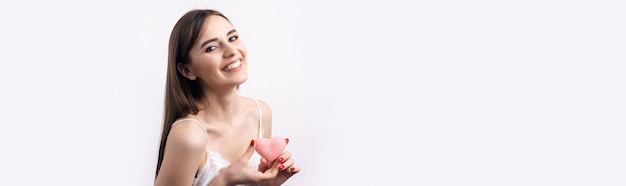 Beautiful smiling woman with clean skin natural makeup and white teeth on a gray background Holding a pink hygienic heart