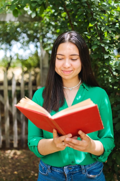 Beautiful smiling young farmer woman reading book in the field. Vertical shot. World book day