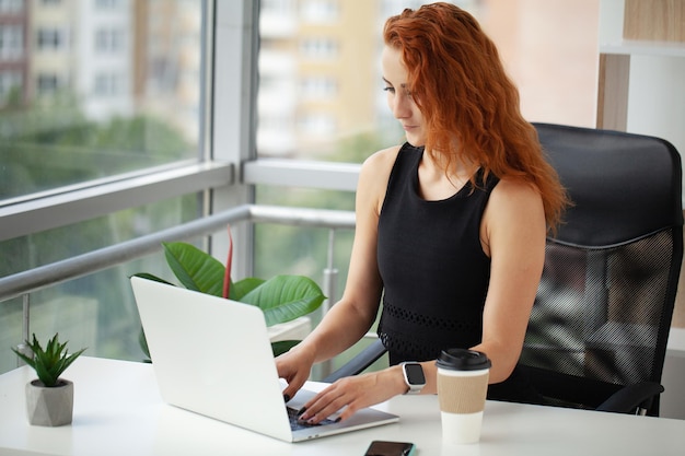 Beautiful smiling young redhaired business lady posing in office