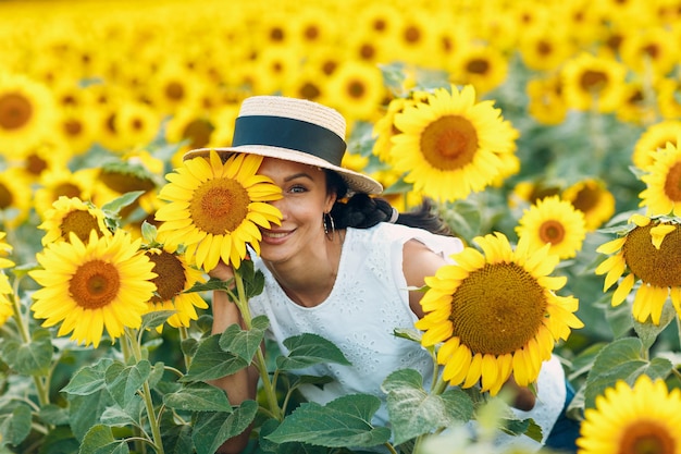 Beautiful smiling young woman in a hat with flower on her eye and face on a field of sunflowers