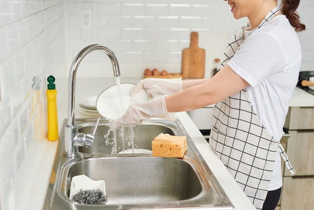 Beautiful smiling young woman washing the dishes in modern white kitchen.