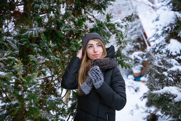 Beautiful smiling young woman in winter outdoors in warm jacket enjoys weather among the snowcovered...