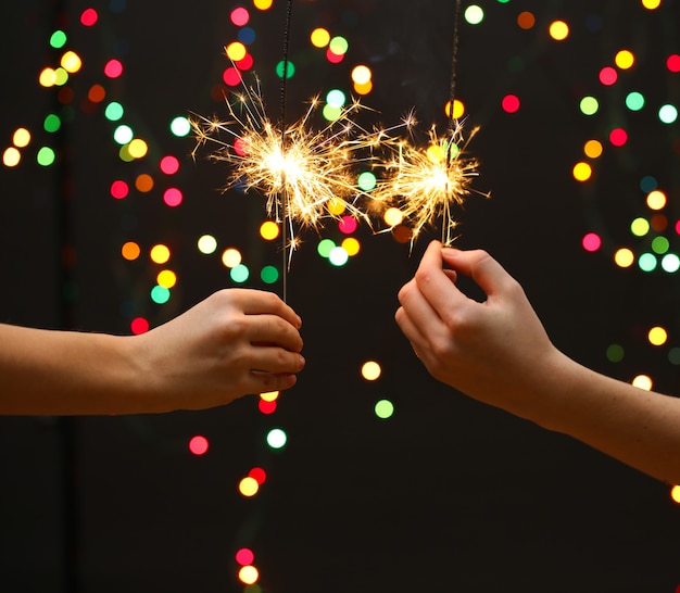 Beautiful sparklers in woman hands on garland background