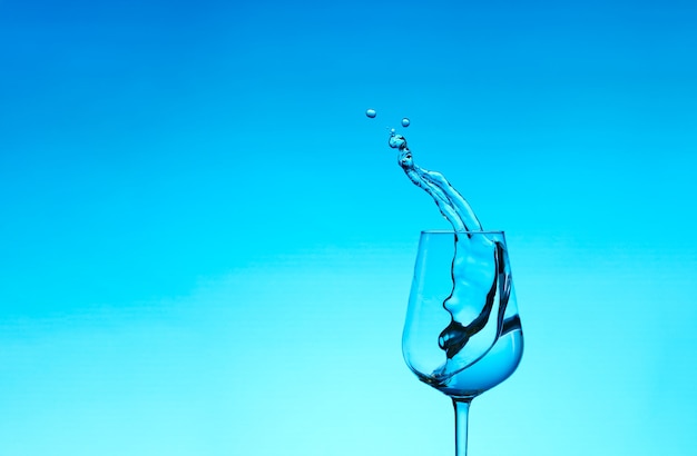 Beautiful splashes of water in a wine glass, with blue filter, close up with copy space.