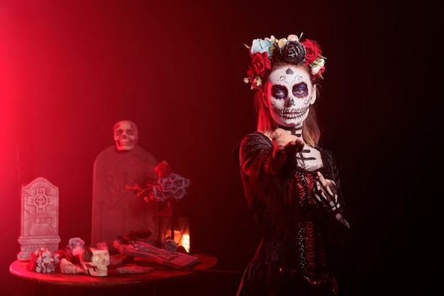 Beautiful spooky adult reaching with hand, trying to lure and tempt victims in studio. Flirty santa muerte model with mexican ritual costume on holiday celebration, day of the dead myth.