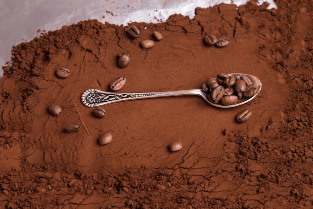 A beautiful spoon with coffee beans lies on the background of ground roasted coffee Food background