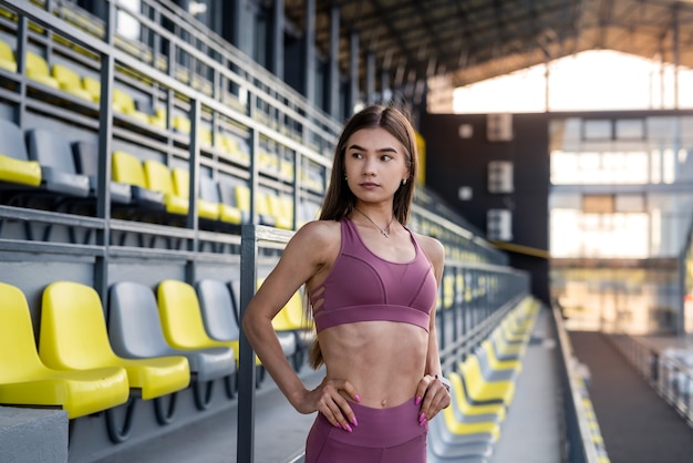 Beautiful sporty girl having rest near on sits on stadium in sunny day