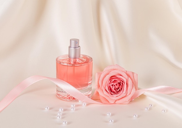 Beautiful still life with a bottle of womens perfume or cosmetic spray on a beige satin background with pink roses and a satin ribbon layout