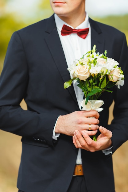 Beautiful strong groom in a suit with a tie, holding a bridal bouquet