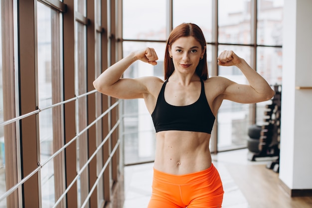 Beautiful strong woman showing her biceps and smiling while working out at gym