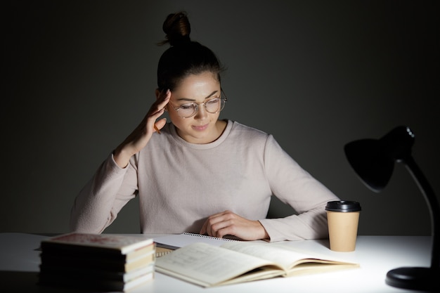 Beautiful student sits at white desk against dark