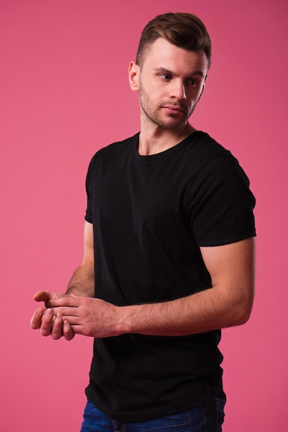 Beautiful stylish confident and serious man in black t-shirt is posing on pink background