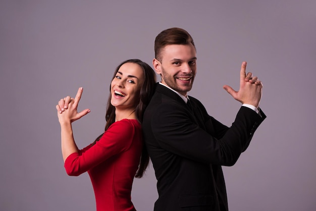 Beautiful stylish and elegant couple in suit and dress are standing back to back, have a fun and posing isolated in studio. Holidays and events. St Valentine's day. Day of lovers