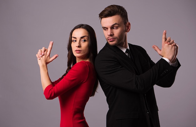 Beautiful stylish and elegant couple in suit and dress are standing back to back, have a fun and posing isolated in studio. Holidays and events. St Valentine's day. Day of lovers