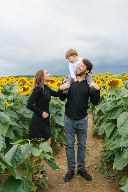 A beautiful stylish family walks in a field of sunflowers Summer lifestyle in the fresh air family leisure with a child