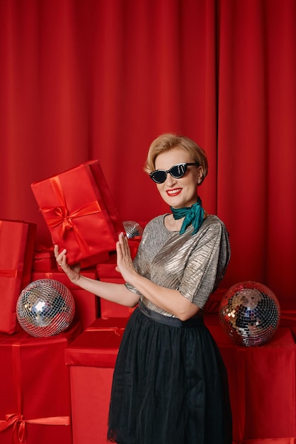 Beautiful stylish mature woman in sunglasses with disco ball and gift box on gift boxes background.