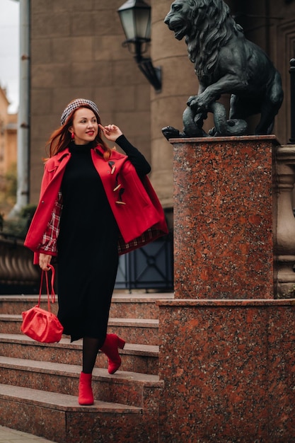 A beautiful stylish woman dressed in an elegant red coat with a stylish red handbag in the autumn city