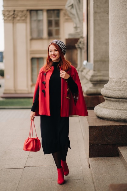 A beautiful stylish woman dressed in an elegant red coat with a stylish red handbag in the autumn city