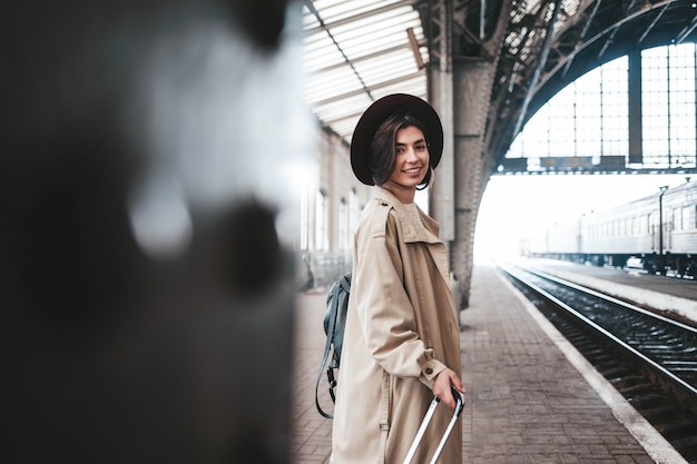 Beautiful stylish woman traveler stands on the person of the station waiting for the train